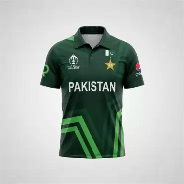 Star Nation Pakistan Cricket Jersey 2023 front view featuring a dark green short-sleeve polo-style cricket shirt with a folded collar, buttoned placket, and geometric green patterning across the fabric. The jersey has large white “PAKISTAN” lettering across the center of the chest, with the Pakistan cricket star emblem and Pakistan flag detail on the upper right chest, and the ICC Cricket World Cup India 2023 tournament logo on the upper left chest. A Pepsi sponsor logo is visible on the right sleeve, while a green sponsor-style emblem appears on the left sleeve. Bright green and darker green angular stripes form a prominent geometric design across the lower front of the jersey, extending diagonally from the sides toward the bottom hem. The jersey is displayed upright against a plain light gray background with even studio lighting, showing the full front design and overall shape of the Star Nation Pakistan Cricket Jersey 2023.