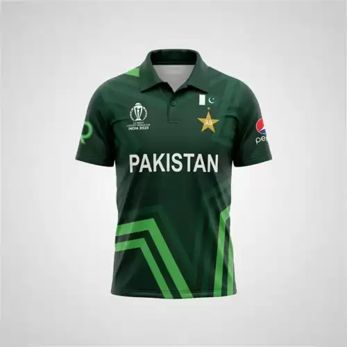 Star Nation Pakistan Cricket Jersey 2023 front view featuring a dark green short-sleeve polo-style cricket shirt with a folded collar, buttoned placket, and geometric green patterning across the fabric. The jersey has large white “PAKISTAN” lettering across the center of the chest, with the Pakistan cricket star emblem and Pakistan flag detail on the upper right chest, and the ICC Cricket World Cup India 2023 tournament logo on the upper left chest. A Pepsi sponsor logo is visible on the right sleeve, while a green sponsor-style emblem appears on the left sleeve. Bright green and darker green angular stripes form a prominent geometric design across the lower front of the jersey, extending diagonally from the sides toward the bottom hem. The jersey is displayed upright against a plain light gray background with even studio lighting, showing the full front design and overall shape of the Star Nation Pakistan Cricket Jersey 2023.
